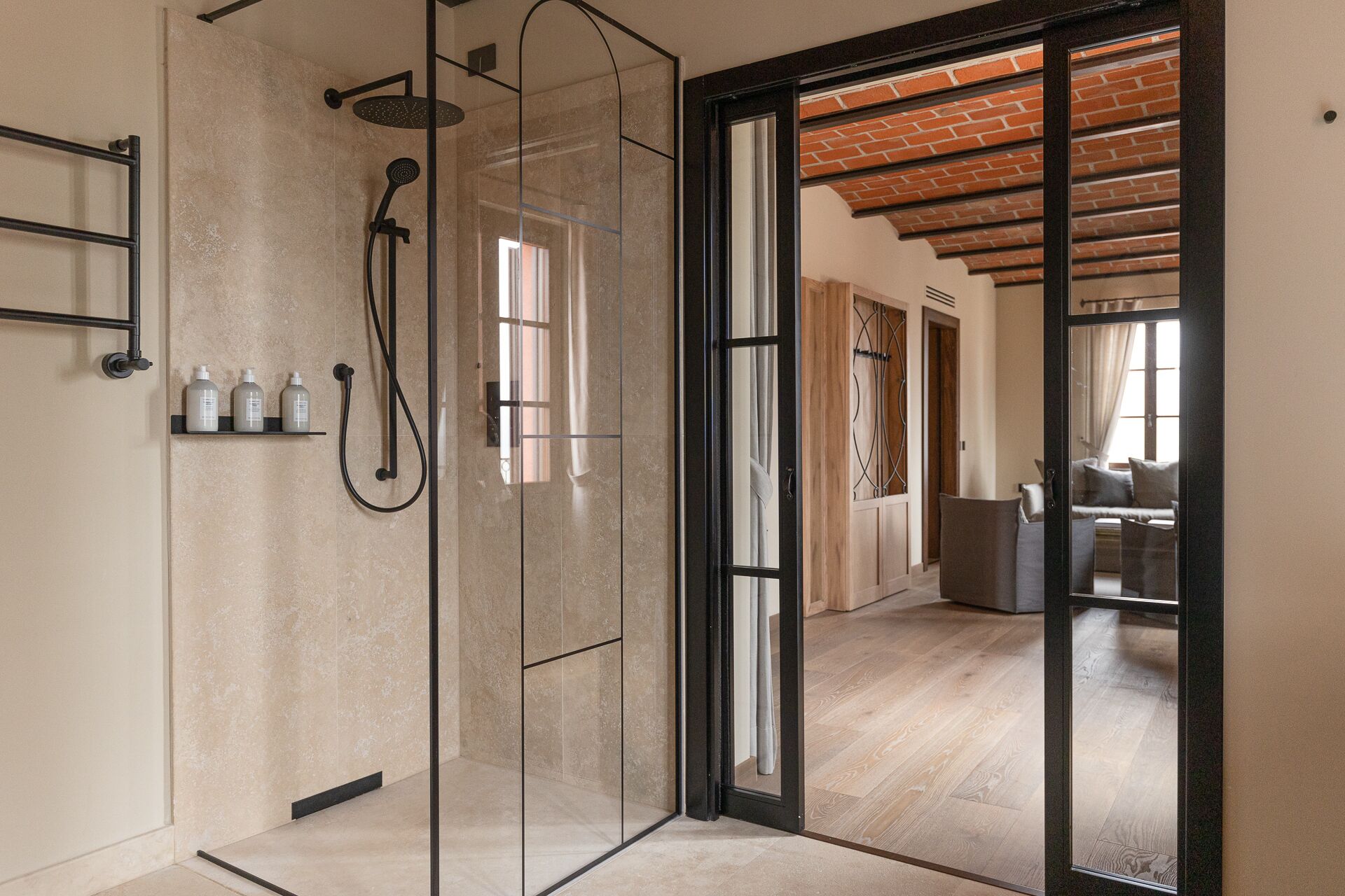 Een moderne badkamer met een douchecabine van glas, een zwarte handdoekhouder en een plank met toiletartikelen.