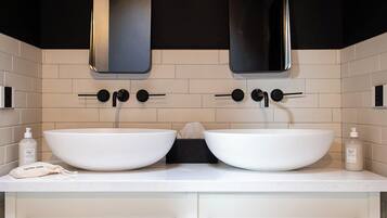 Un baño moderno con dos lavamanos blancos, grifos negros y techo de madera.