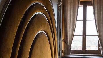 A bed with a curved headboard, a window with curtains, and a brick wall in the background.