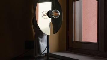 A desk lamp with a reflective surface, positioned on a desk near a window with a view of a building.
