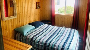 Une pièce aux murs lambrissés, comprenant un lit, une petite table, un miroir et une fenêtre avec des rideaux.