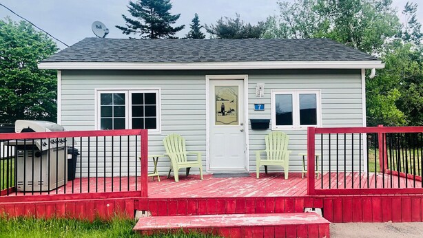 Une petite maison de plain-pied avec un porche rouge et deux fauteuils Adirondack verts.