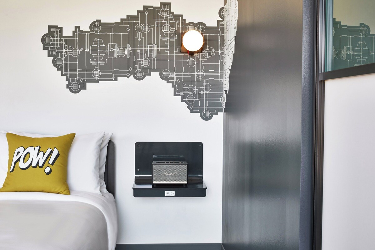 A hotel room with a bed, a wall-mounted speaker, and a wall decal.