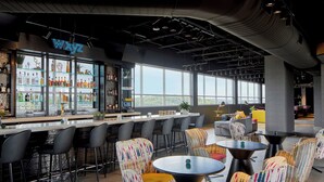 A modern bar area with a bar counter, seating, and a large window offering a city view. - Aloft by Marriott Chattanooga Hamilton Place (Chattanooga)