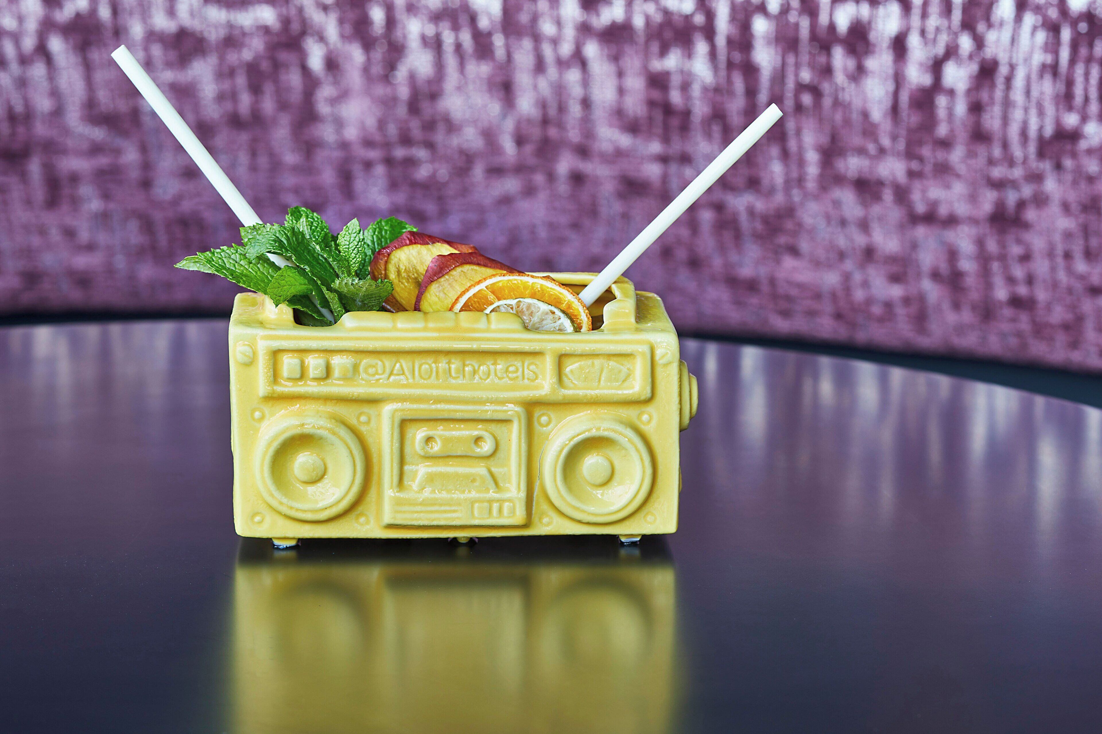 Un recipiente amarillo con forma de coche de juguete, con pajita y hojas de menta.