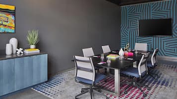 Una sala de conferencias moderna con una mesa grande, cuatro sillas, un televisor montado en la pared y una alfombra estampada.