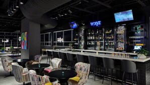 A modern bar area with a long counter, multiple bar stools, and a variety of seating options including round tables and chairs. - Aloft by Marriott Chattanooga Hamilton Place (Chattanooga)