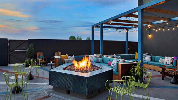 An outdoor seating area with a fire pit, green chairs, and a blue pergola with string lights. - Aloft by Marriott Chattanooga Hamilton Place (Chattanooga)