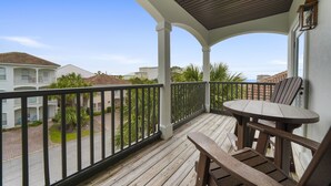 Une terrasse en bois avec une table et des chaises, une rambarde et une vue sur les bâtiments et la végétation environnants.