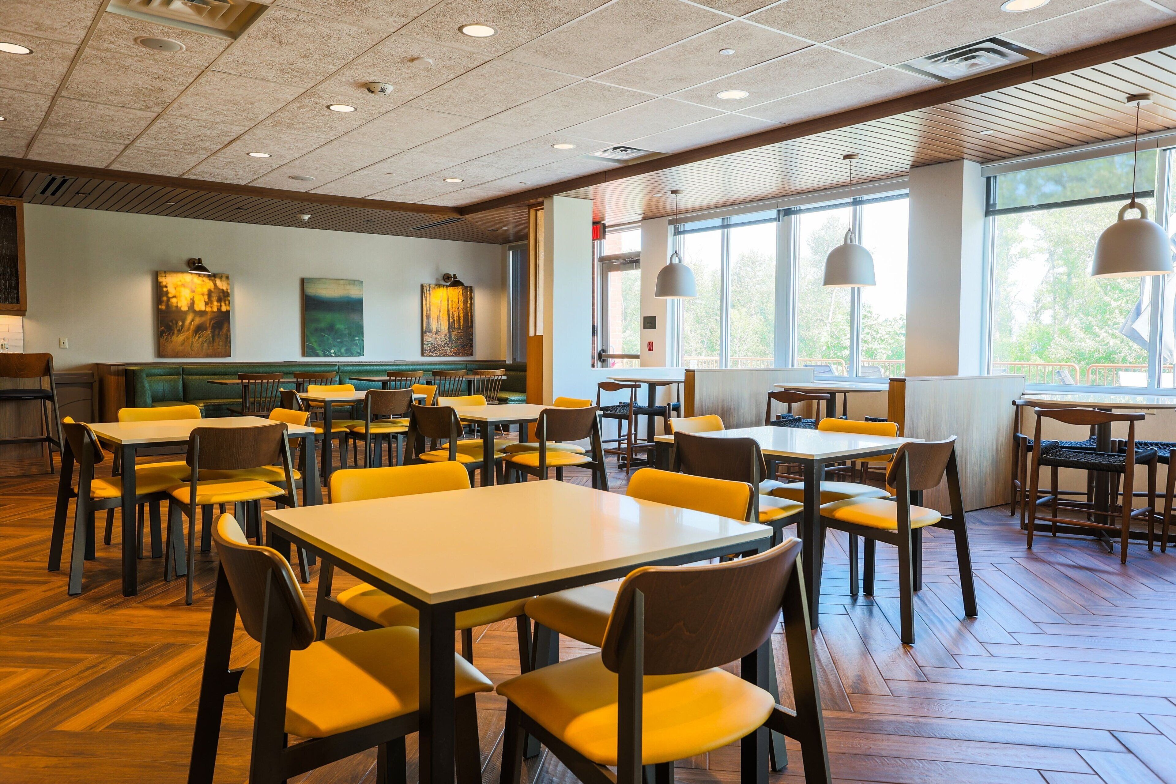 A spacious dining area with multiple tables and chairs, large windows, and artwork on the walls.