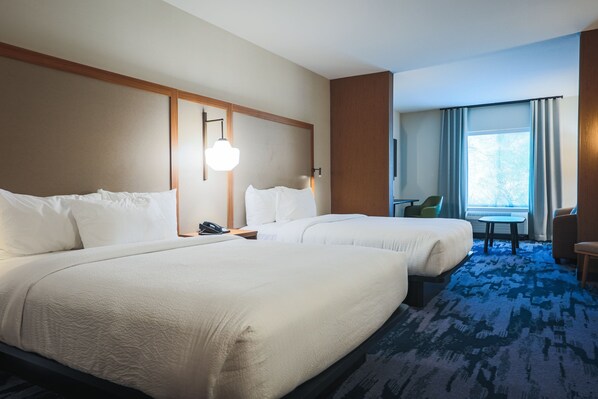 A hotel room with two beds, a desk, a chair, and a window with curtains.