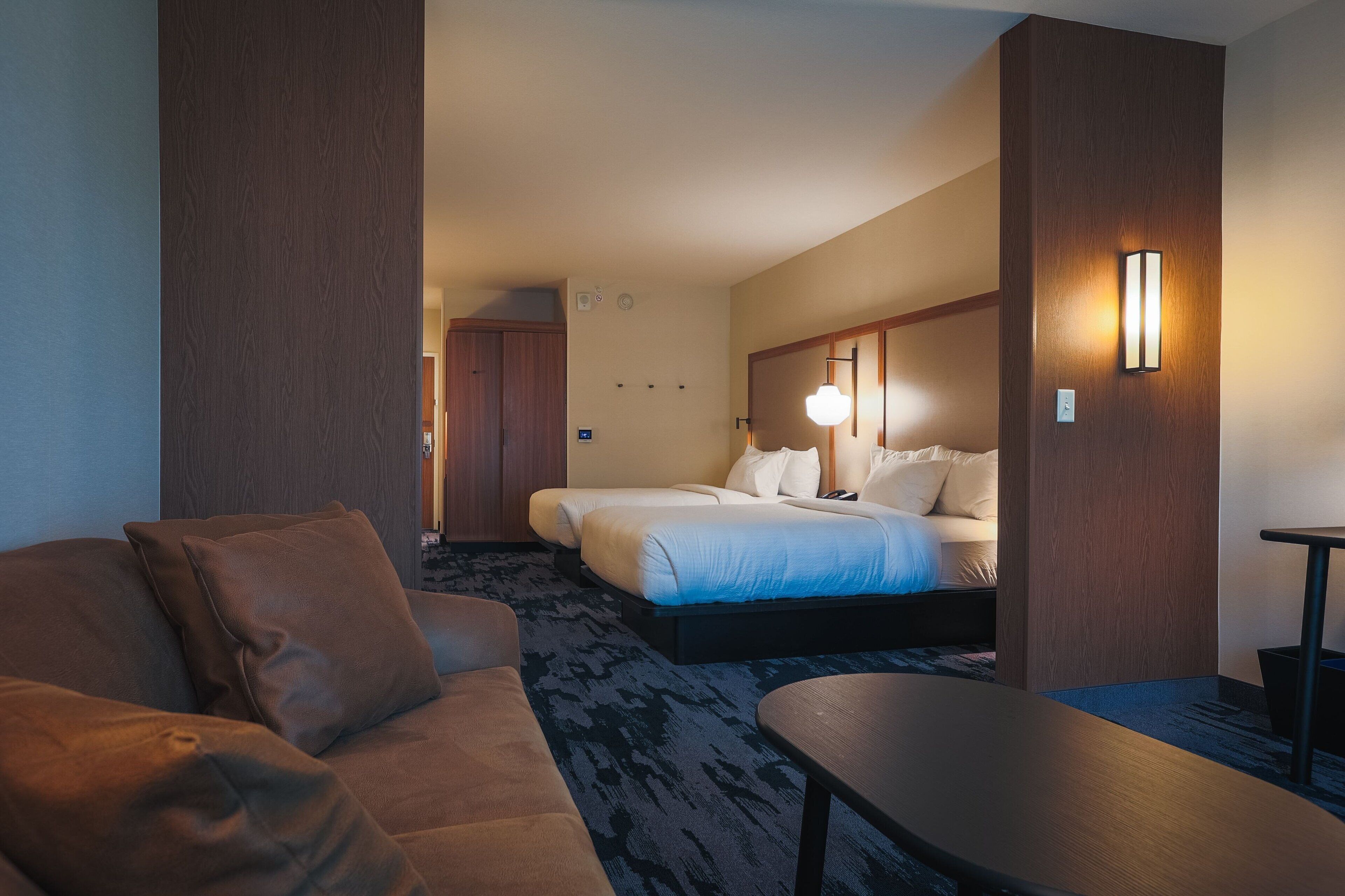 A hotel room with a bed, a sofa, a small table, and a wall-mounted lamp.