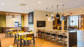Un restaurant moderne avec un plancher en bois, des chaises jaunes, un coin bar et des luminaires suspendus.