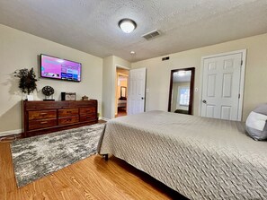 A bedroom with a bed, dresser, TV, and a door leading to another room.