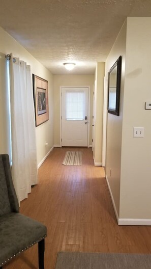 A hallway with a door, a framed picture, a chair, and a rug.
