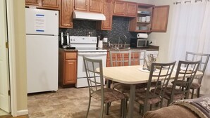 Cocina compacta con muebles de madera, un refrigerador blanco, una estufa y una mesa de comedor con sillas.