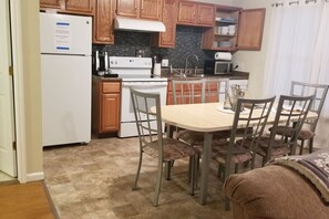 A compact kitchen with wooden cabinets, a white refrigerator, a stove, and a dining table with chairs.
