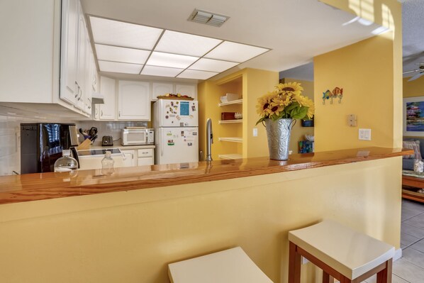 Una cocina con armarios blancos, encimera de madera y un jarrón con girasoles.