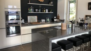 A modern kitchen with built-in appliances, a central island with bar stools, and a black backsplash. - Remarkable 4-bed Villa in Bellano (Bellano)