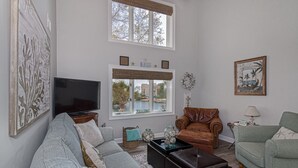 A living room with a grey sofa, a brown leather armchair, a green armchair, a flat-screen TV, and a window with a view of the outdoors. - One of kind 3 bedroom Villa with Ocean/Lagoon Views. (Hilton Head Island)