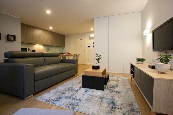 A modern living room with a grey sofa, a coffee table, and a TV mounted on the wall.