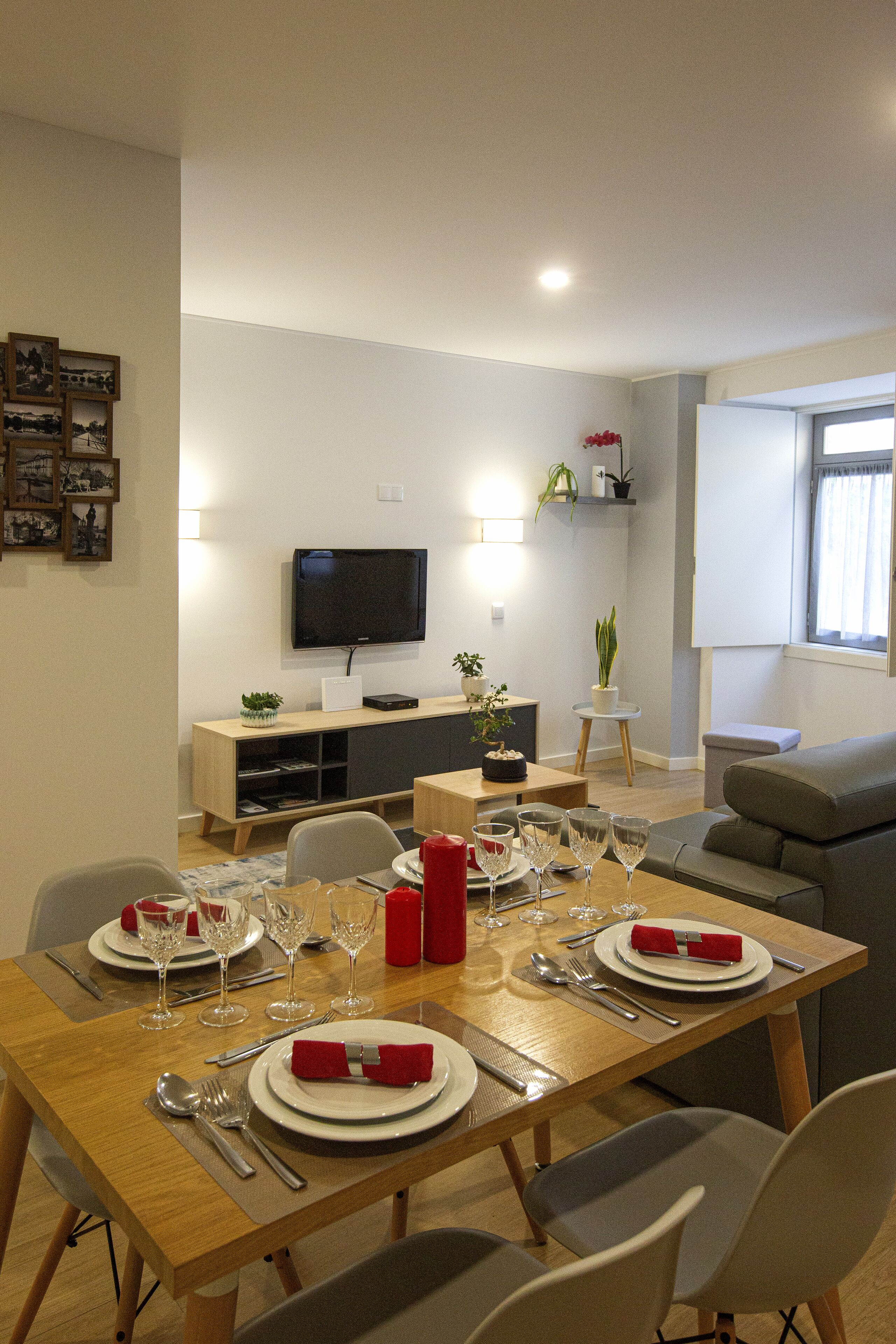 Ein Essbereich mit einem Holztisch, gedeckt für vier Personen, einem an der Wand montierten Fernseher und einem grauen Sofa im Hintergrund.