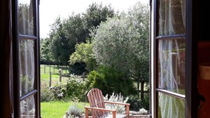 An open door with a view of a garden, a wooden chair, and a table outside. - Landes" guest room with private Nordic bath (Sigalens)