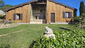 A wooden building with a stone foundation, a large open entrance, and a grassy yard with a stone sculpture. - Landes" guest room with private Nordic bath (Sigalens)