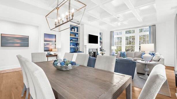 A modern dining area with a wooden table, white upholstered chairs, and a decorative chandelier. - Penthouse in popular, centrally located new construction neighborhood (Kiawah Island)