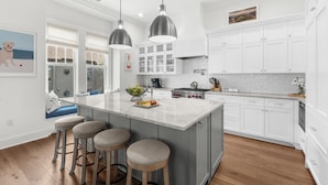 A modern kitchen with white cabinetry, a large island with stools, pendant lighting, and a view to the outside. - Penthouse in popular, centrally located new construction neighborhood (Kiawah Island)