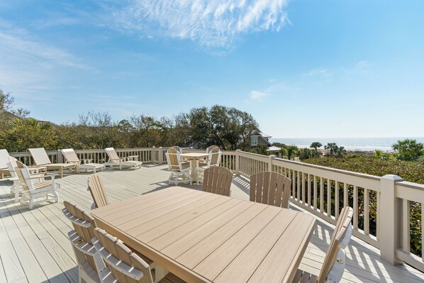 A wooden deck with outdoor furniture, a table, and chairs, overlooking a beach and ocean.