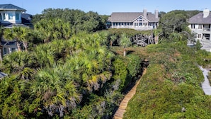 A coastal property with a wooden boardwalk, lush greenery, and multiple houses with distinct architectural styles. - Beachside Treehouse, spectacular ocean view on popular Surfsong Rd (Kiawah Island)
