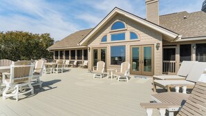 A covered deck with outdoor seating and a building with large windows. - Beachside Treehouse, spectacular ocean view on popular Surfsong Rd (Kiawah Island)