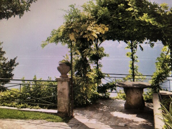 Un jardín con un banco de piedra, un pérgola y una fuente de agua.