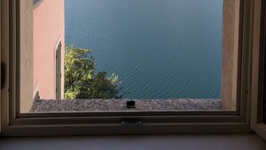 A view through a window of a building with a pink facade, overlooking a lake with mountains in the background. - Villa Giudici Luxury app on the Lake (Nesso)