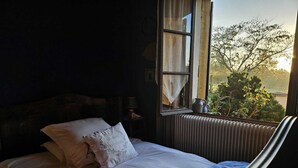 Quarto com cama, janela com vista para vegetação e radiador.