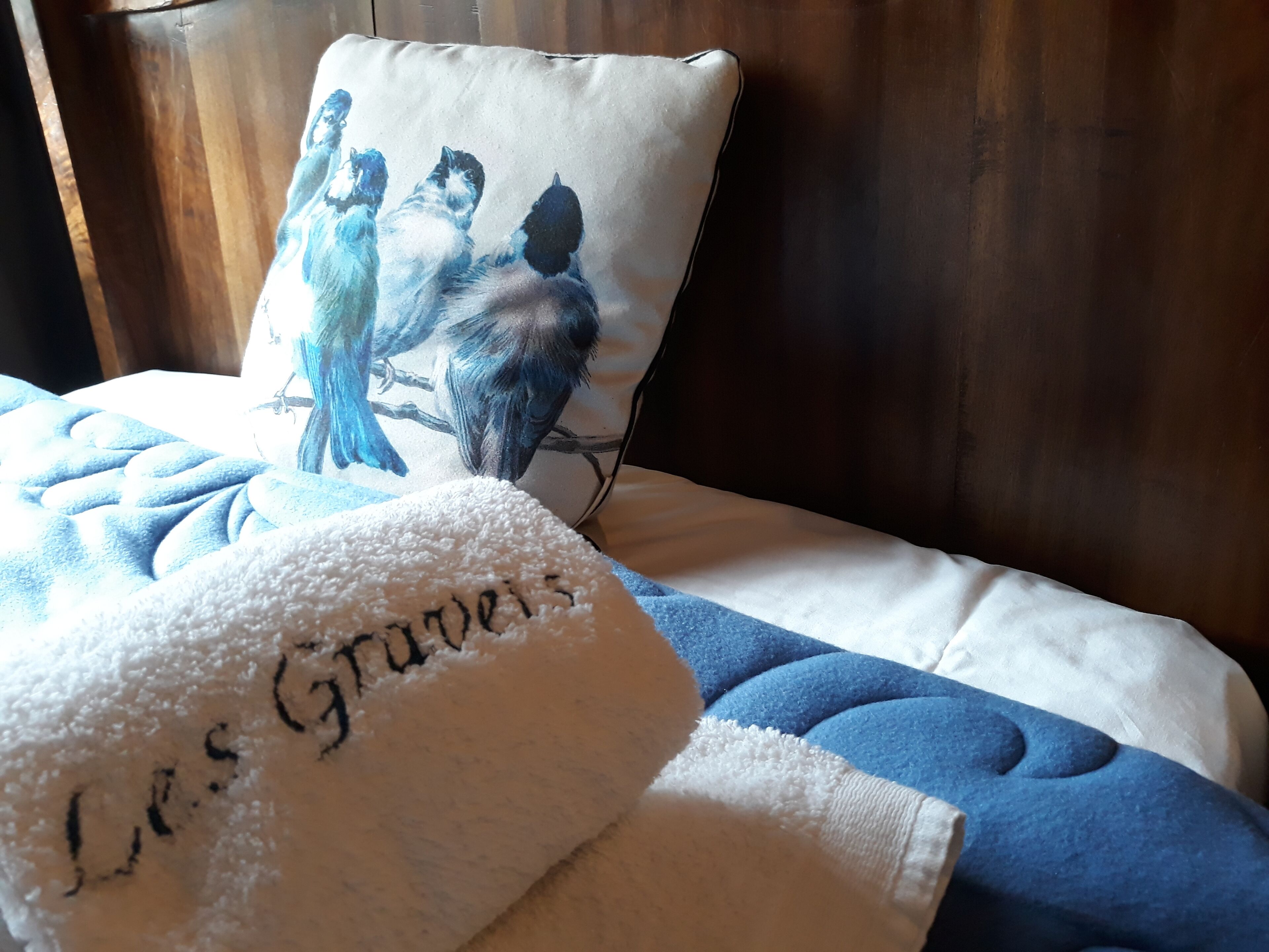 Ein Bett mit einer blauen Decke, einem weißen Kissen mit Vogelmotiv und einem weißen Handtuch mit Aufdruck.