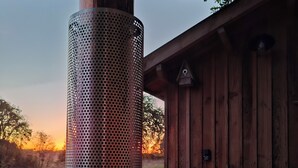 Uma banheira de hidromassagem com coluna metálica perfurada, deck de madeira e vista para o pôr do sol.