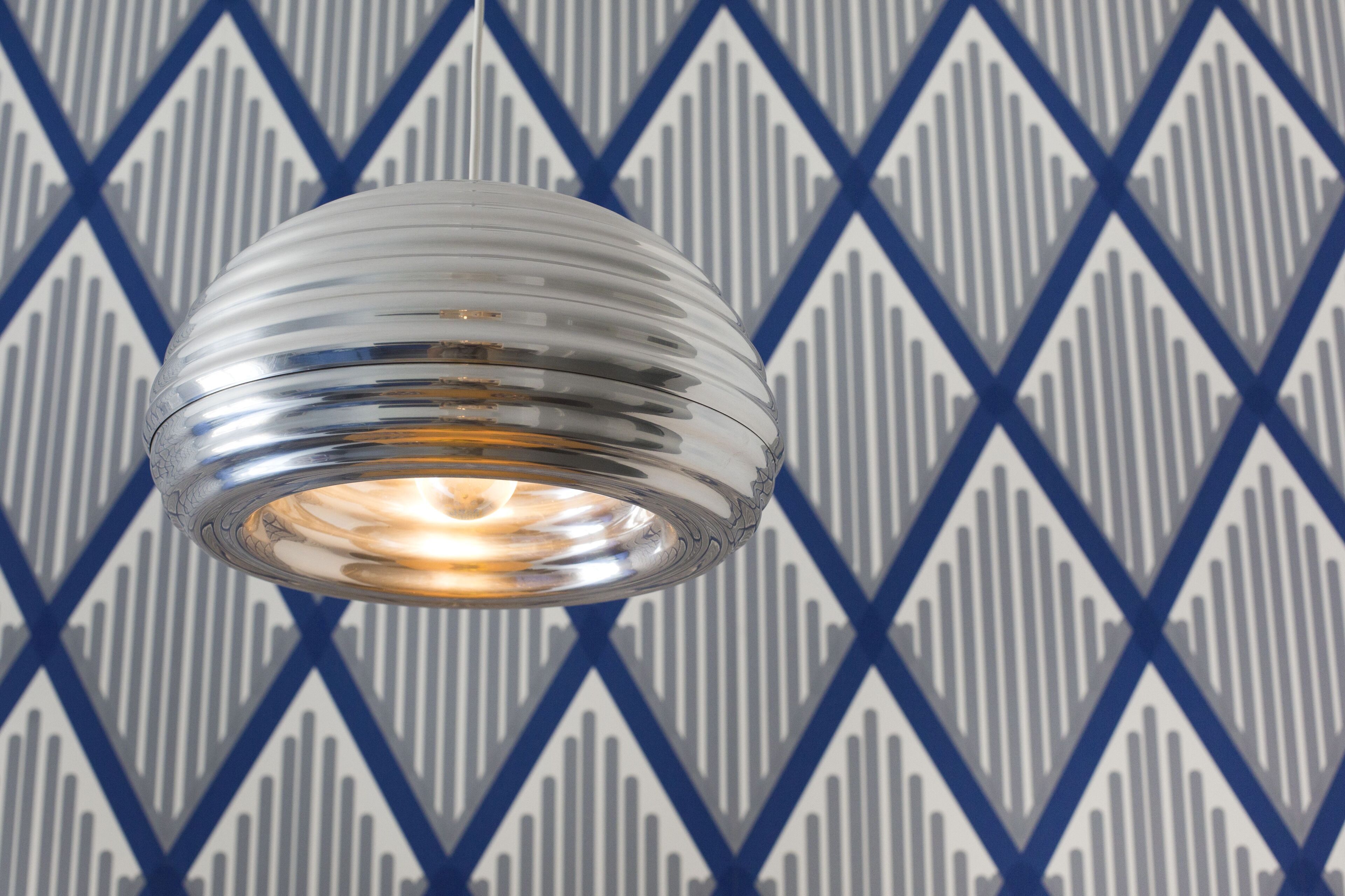 A metallic, ribbed light fixture against a patterned wall.