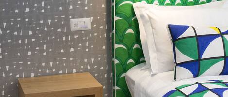 A bedroom with a green patterned headboard, a bedside table with books, and a lamp.