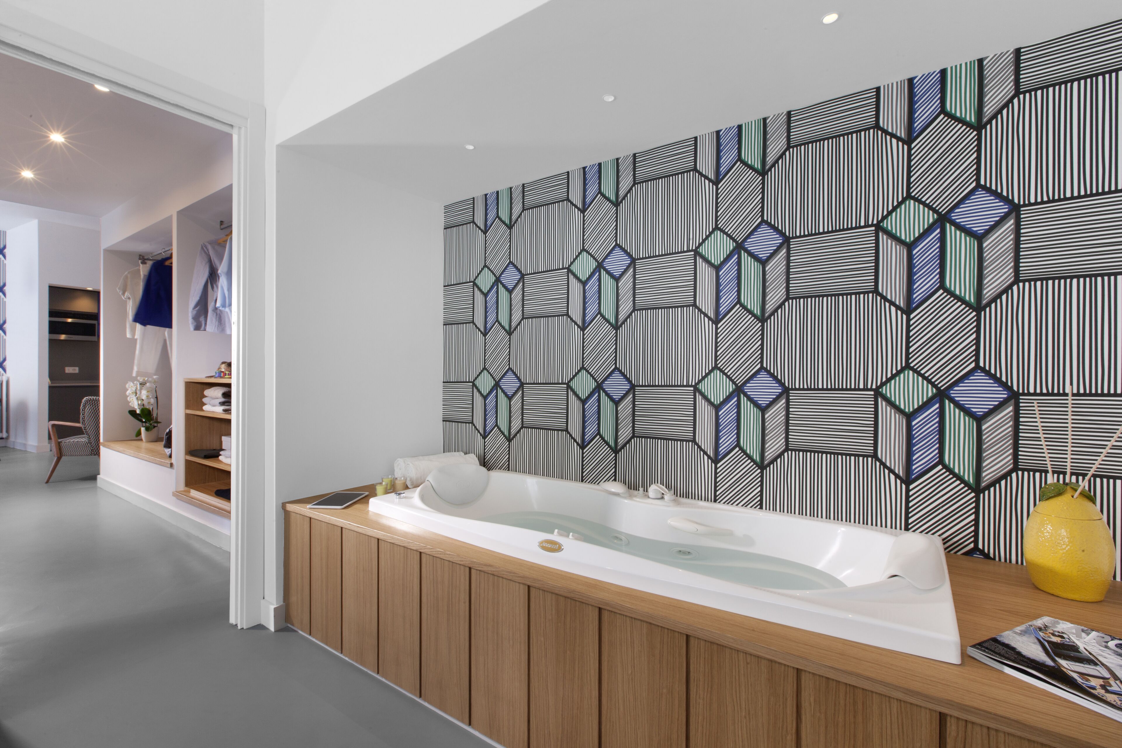 A modern bathroom with a freestanding bathtub, wooden vanity, and a geometric-patterned wall.