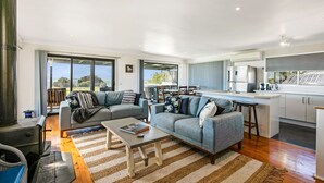 A modern living room with a sofa, coffee table, and a kitchen area with a refrigerator and dining table. - Goku's Shack - Rural and water views with a spa (CORONET BAY)