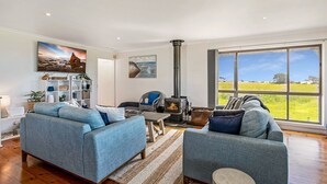 A spacious living room with a large window, a fireplace, and a view of the countryside. - Goku's Shack - Rural and water views with a spa (CORONET BAY)
