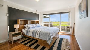 A bedroom with a wooden bed, a nightstand, a lamp, a large window with a view of the outdoors, and a hanging chair. - Goku's Shack - Rural and water views with a spa (CORONET BAY)