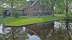 A two-story brick house with a sloped roof, a small front garden, and a pond in the foreground. - Chiristinahoeve De kasteel #7 (Boskoop)