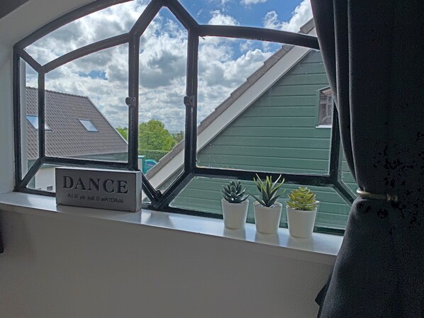 A window with a sign reading "DANCE AS IF NO ONE IS WATCHING" and three potted plants on the windowsill.