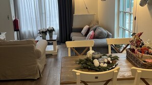 A cozy living room with a dining table set for four, a sofa, a coffee table, and a fireplace. - Christinahoeve Hooiberg #5 (Boskoop)