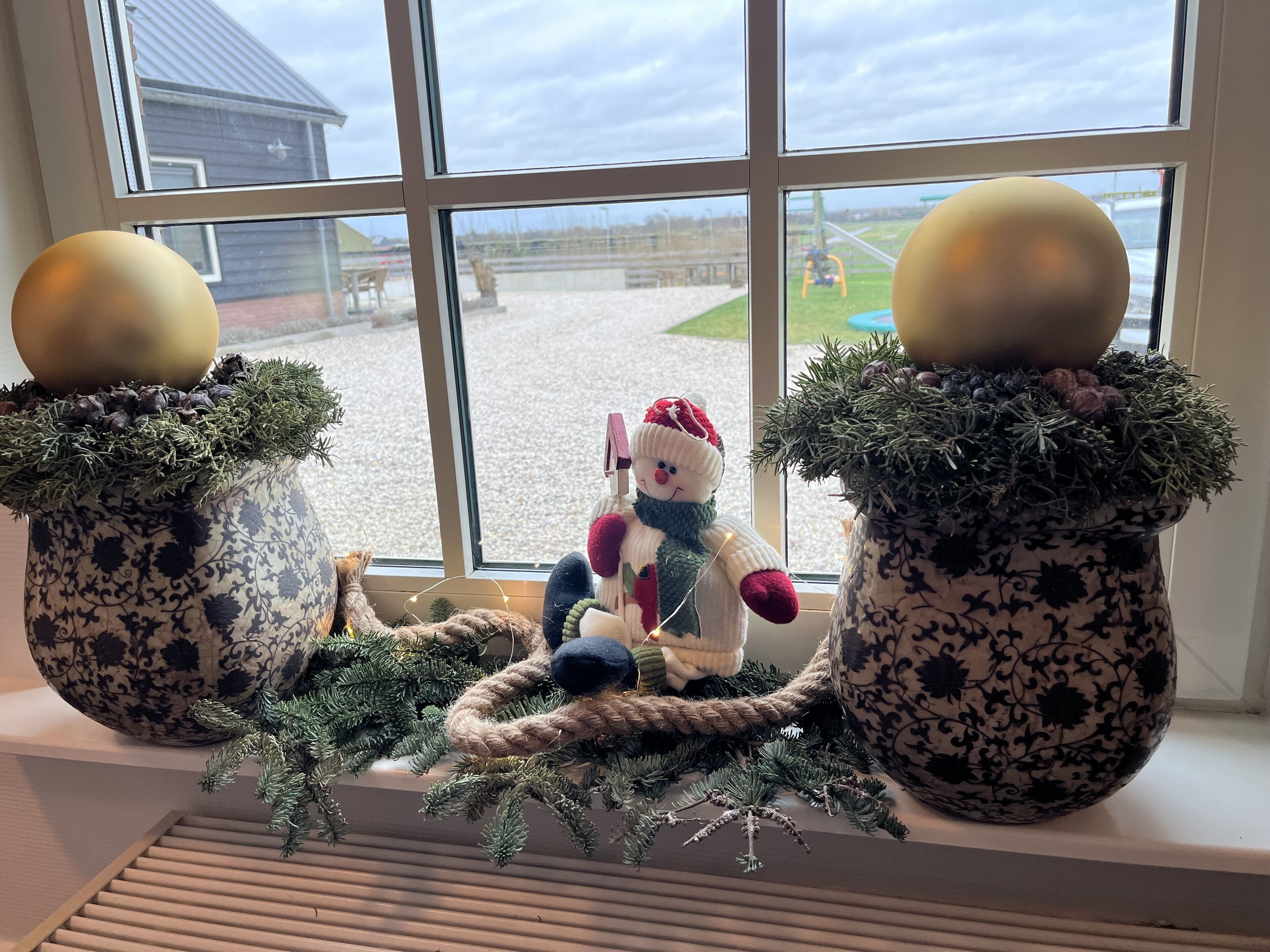 A window with two decorative pots containing Christmas ornaments and a plush toy.