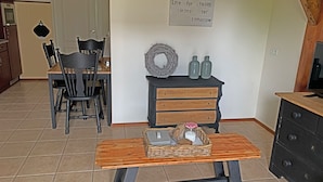 A dining area with a wooden table, chairs, a wall-mounted sign, a decorative wreath, and a dresser with bottles. - Christinahoeve Oude Deel #1 (Boskoop)