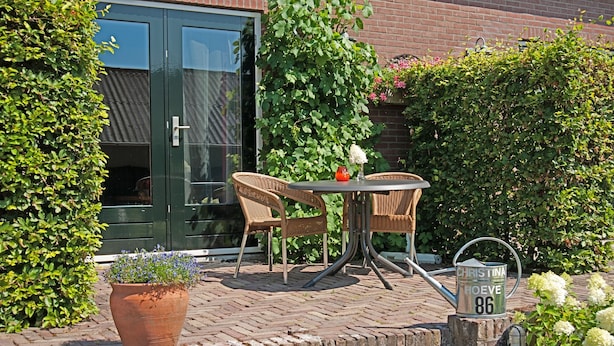 An outdoor patio with wicker chairs, a table, a potted plant, and a metal sign with a name and number. - Christinahoeve Oude Deel #1 (Boskoop)
